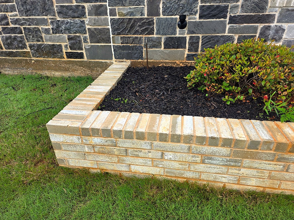 Freshly cleaned brick planter wall beside a mulched bed and stone exterior