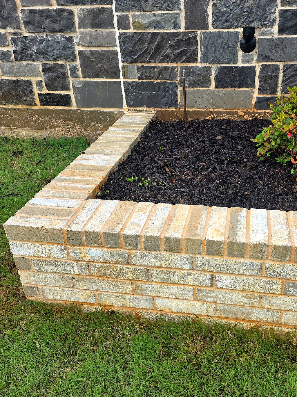 Freshly cleaned brick planter wall and mulched bed beside a stone exterior