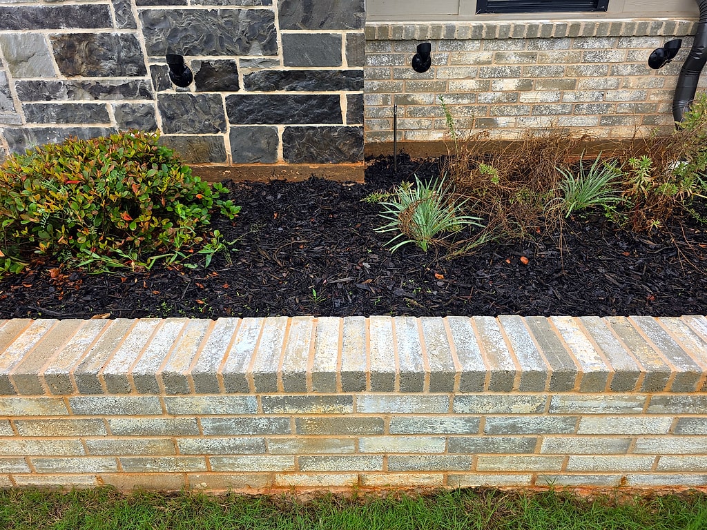 Cleaned brick retaining wall running along a mulched bed beside a stone and brick exterior